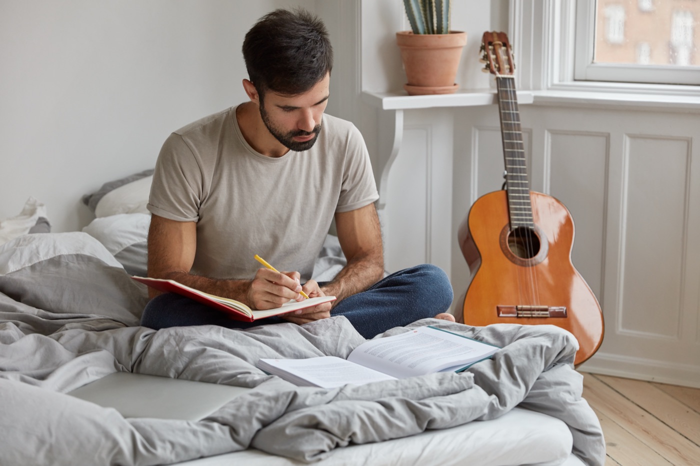 A man in a plain gray T-shirt taking notes from a book