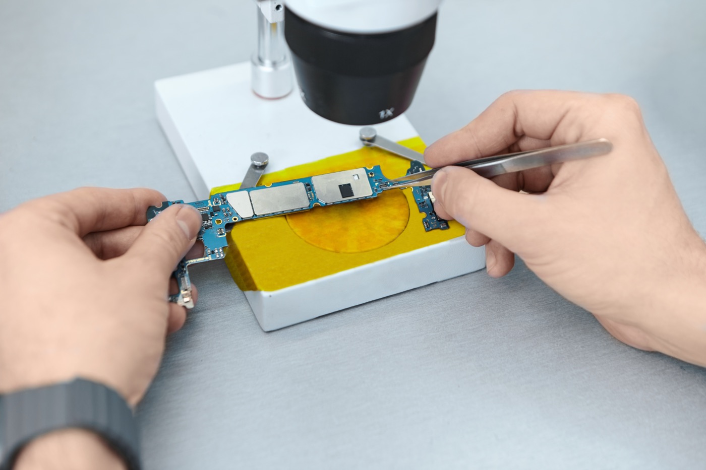 A technician repairing an electronic circuit board under a microscope