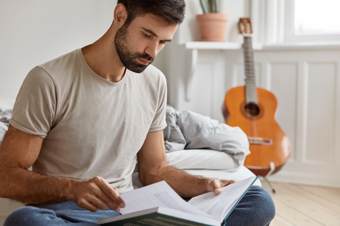 A man in a plain gray T-shirt reading at home