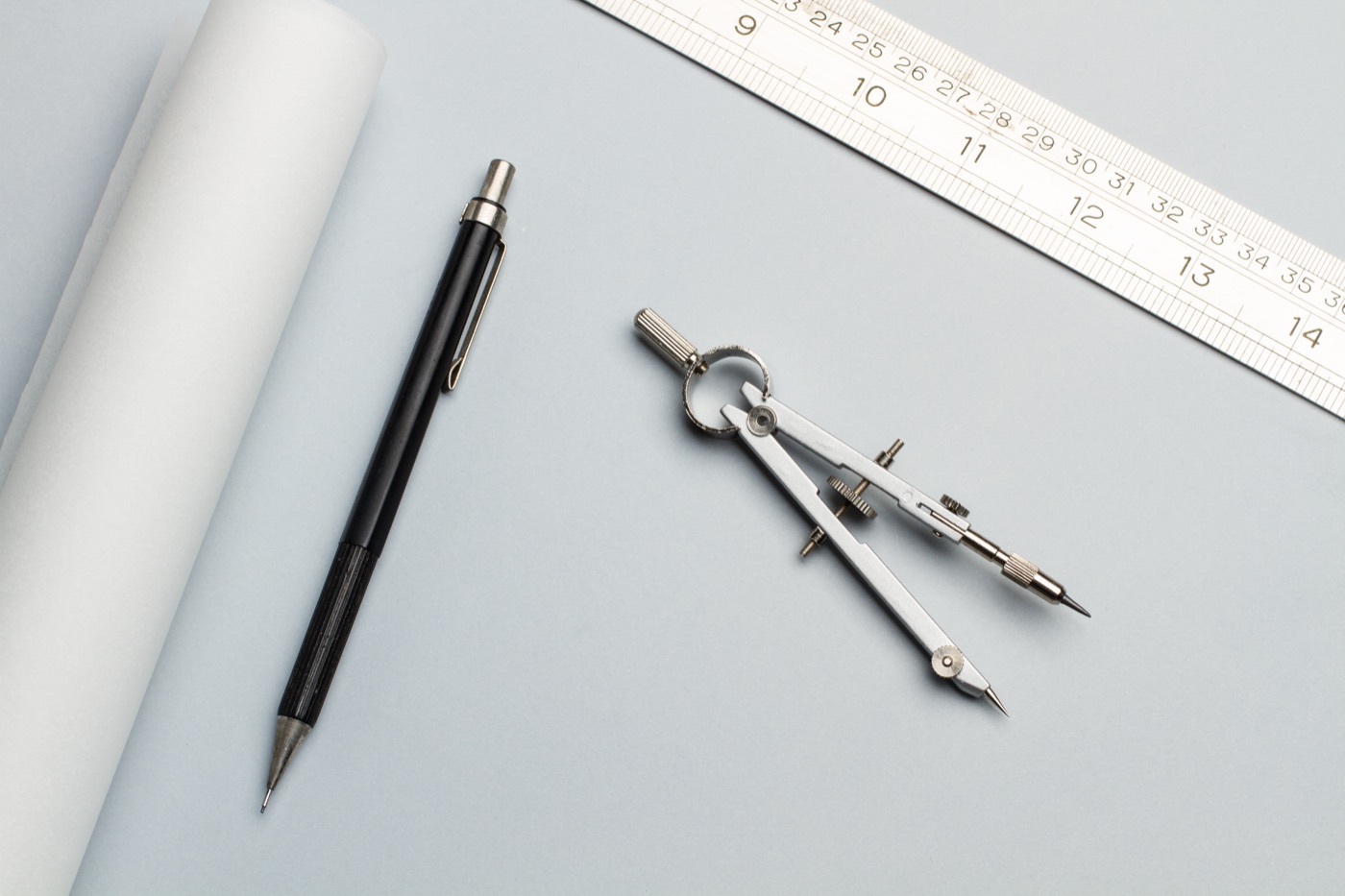 A compass, ruler, and pencils on a gray work surface