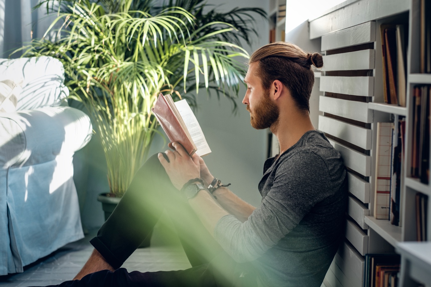 A man in a simple dark shirt reading beside a window