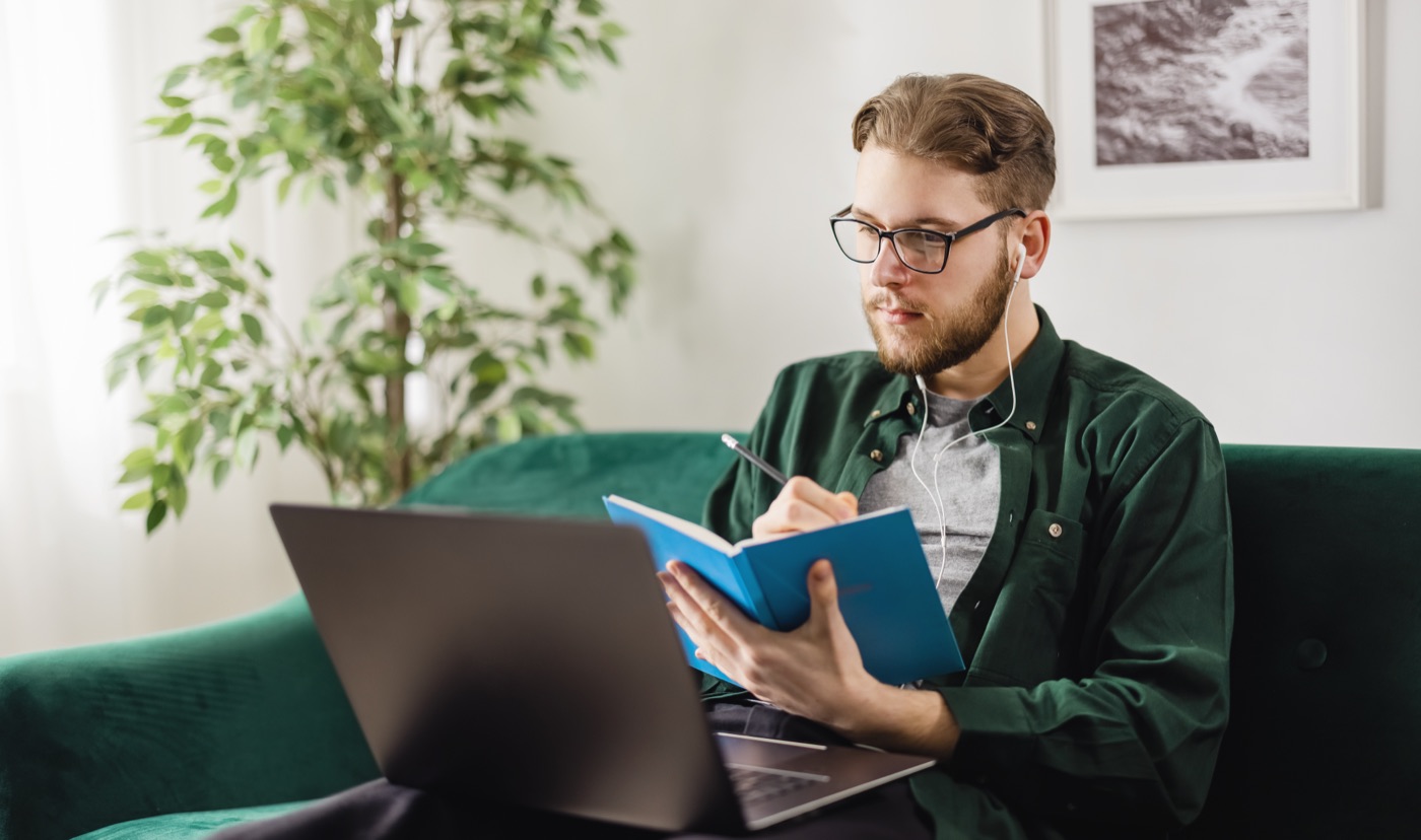 A man in a green overshirt studying with a book and laptop