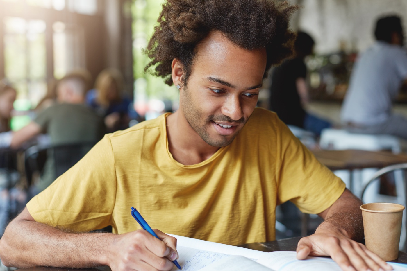 A male student in a yellow T-shirt writing study notes