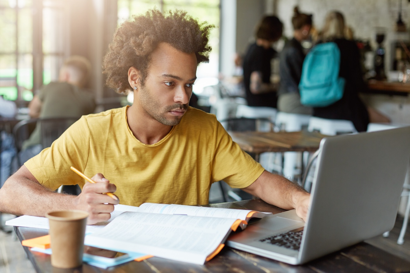 A male student in a yellow T-shirt studying with books and a laptop